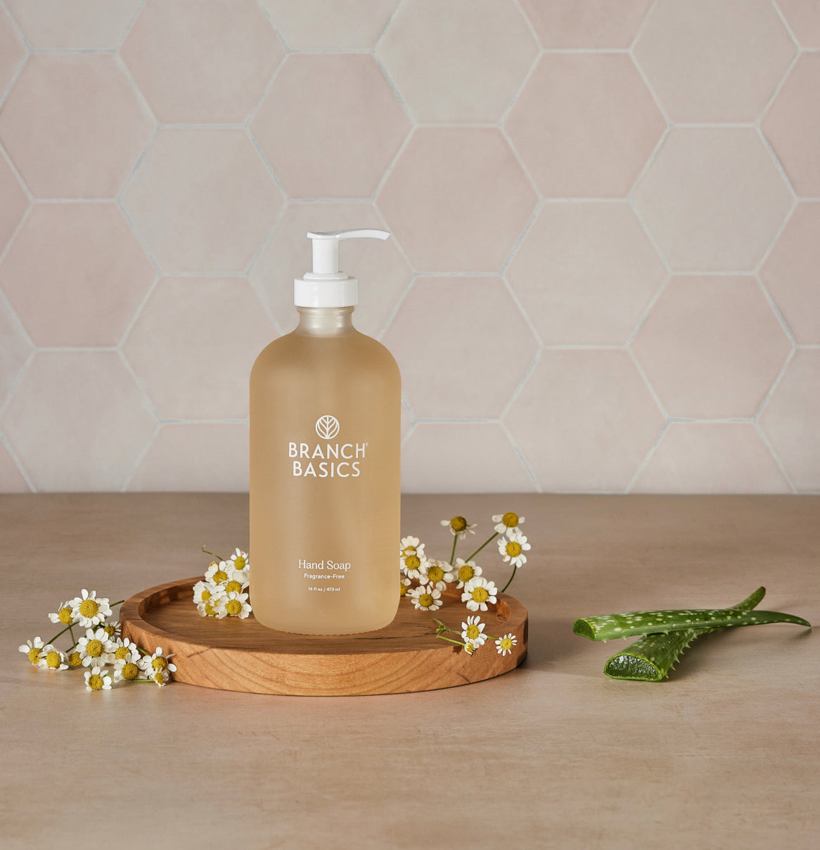 Branch Basics Hand Soap bottle on a wooden pedestal with chamomile and aloe surrounding it.