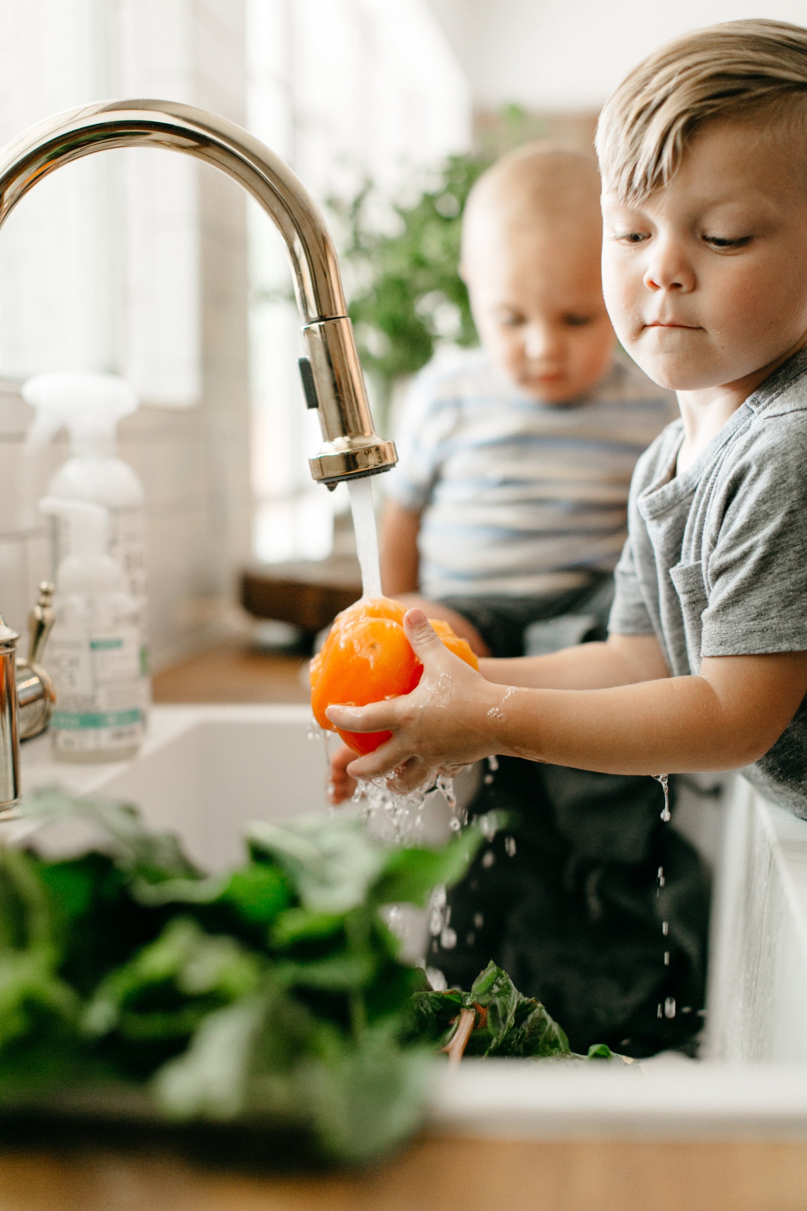 Children rinsing an orange of dirt at the kitchen sink