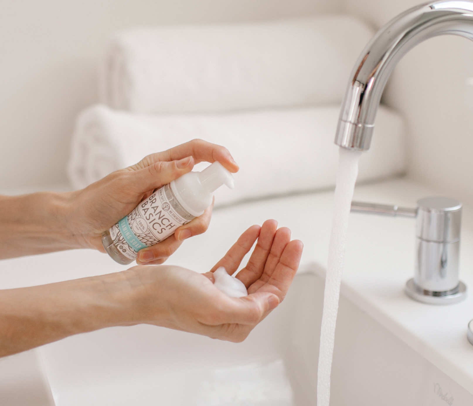 A person standing at a sink, using the mini Foaming Wash bottle to dispense foaming soap into their hands. - View 3
