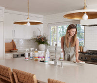 The Premium Starter Kit featuring plastic bottles displayed on a kitchen counter with a woman wiping the counter with a hand towel. - Thumbnail View 6
