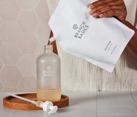 A pouch of Branch Basics Gel Hand soap being used to refill a glass bottle. - Thumbnail View 2

