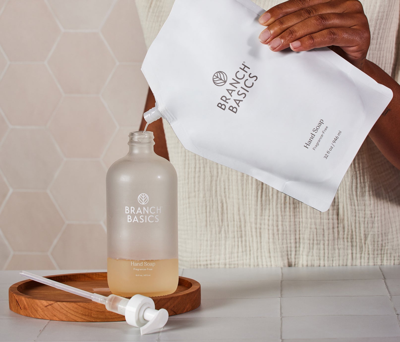 A pouch of Branch Basics Gel Hand soap being used to refill a glass bottle. - View 2
