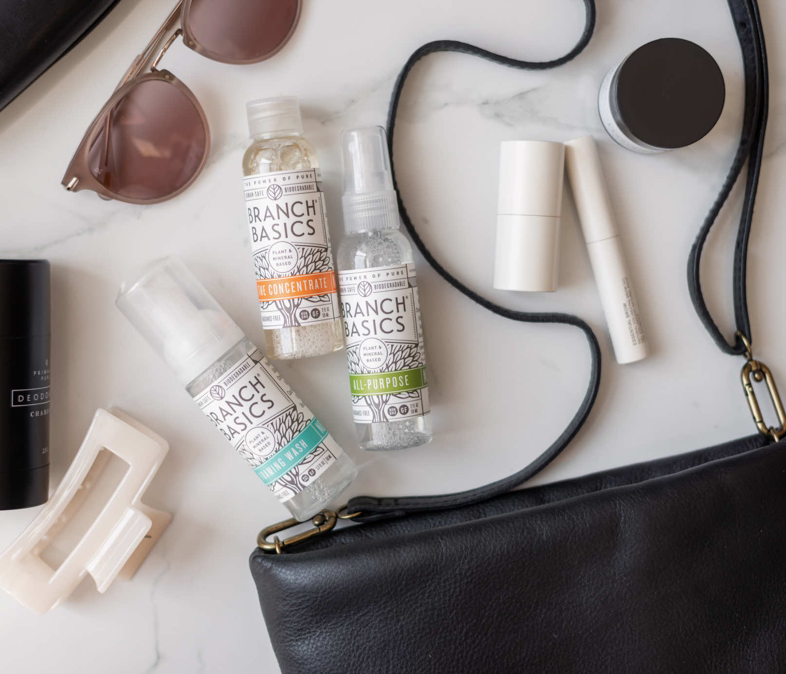 The Travel Kit, featuring mini-versions of the Branch Basics Concentrate, All-Purpose spray, and Foaming Wash pump, displayed on a neutral background, spilling-out from a purse. - View 5
