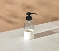 A single refillable Glass Foaming Wash Bottle with a Matte-Black pump, displayed on a white tiled surface and a neutral background. - Thumbnail View 2
