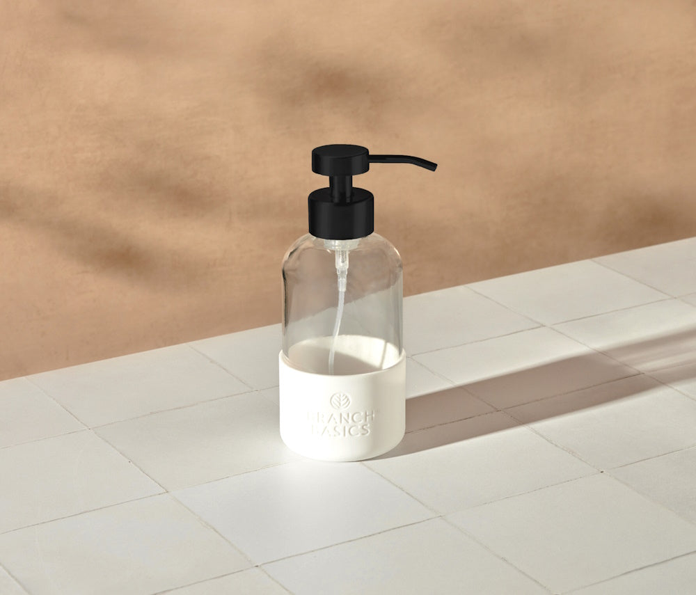A single refillable Glass Foaming Wash Bottle with a Matte-Black pump, displayed on a white tiled surface and a neutral background. - View 2
