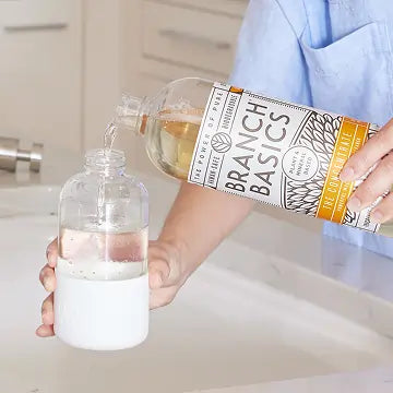 Person pouring Branch Basics Concentrate into a clear glass bottle in a kitchen.