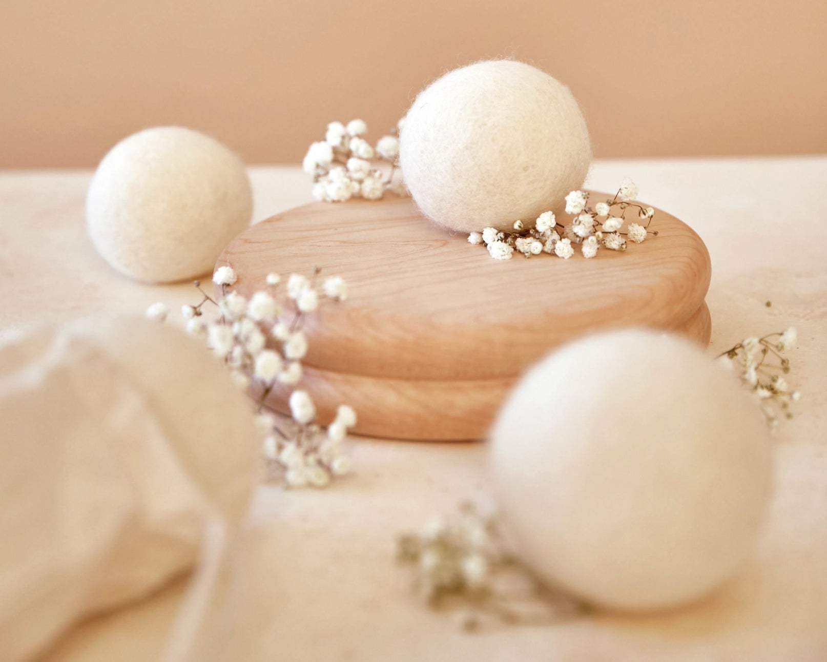 Multiple Wool Dryer Balls are pictured, with the two in the foreground out of focus, the one in the background partially-in-focus, and the one in the midground in-focus and elevated on a wooden tray. - View 3
