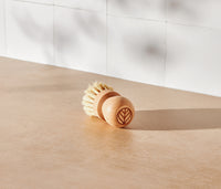 A Natural Scrub Brush, made with a solid beechwood handle and natural fiber bristles, displayed on a neutral surface and white tiled background. - Thumbnail View 2
