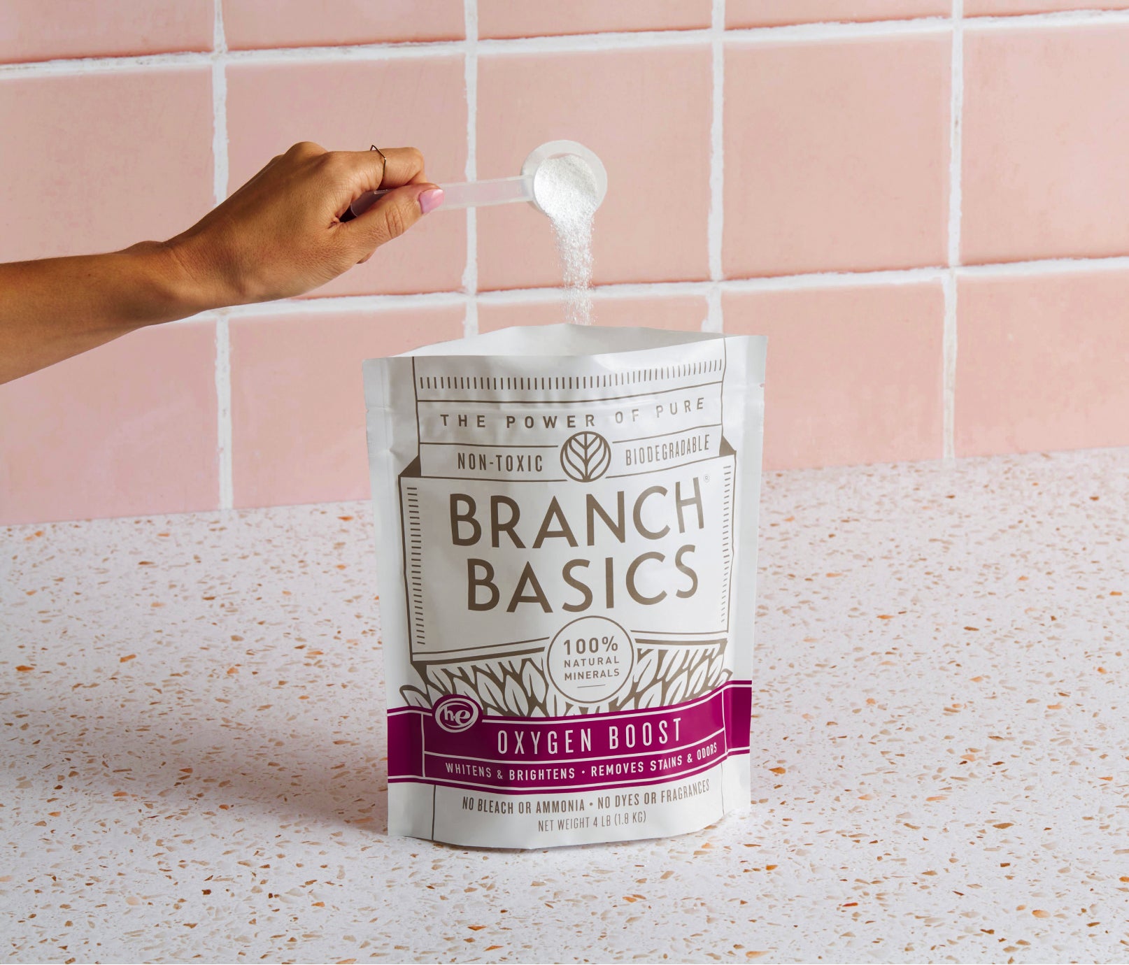 An open pouch of Branch Basics Oxygen Boost; a person is pouring a scoop of the white, granular product back into the original container. - View 2
