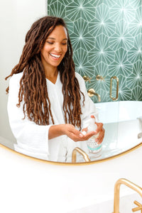 A person shown in a mirror standing at a sink, using a refillable Plastic Foaming Wash Bottle to dispense soap into their hands. - Thumbnail View 3
