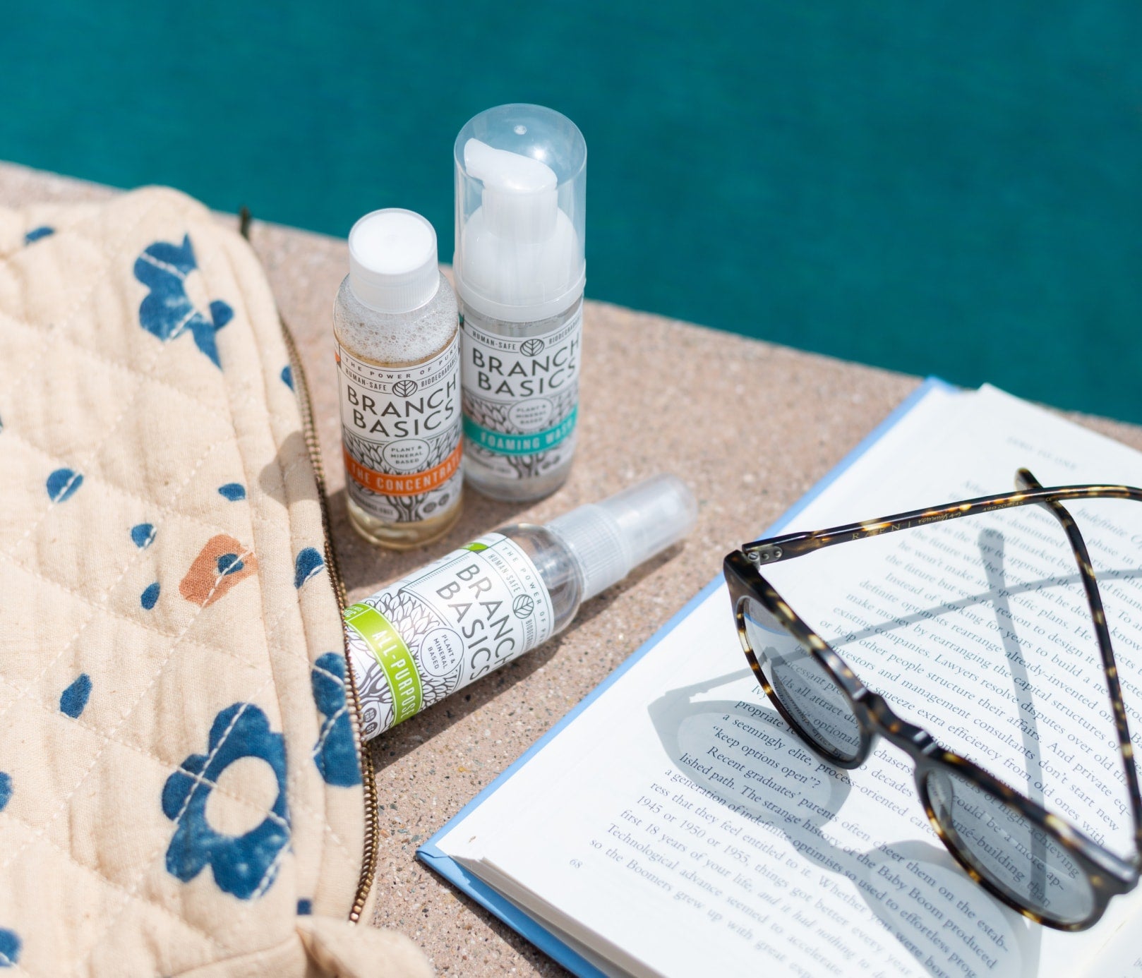 The Travel Kit, featuring mini-versions of the Branch Basics Concentrate, All-Purpose spray, and Foaming Wash pump, displayed poolside, next to an open book and sunglasses. - View 4
