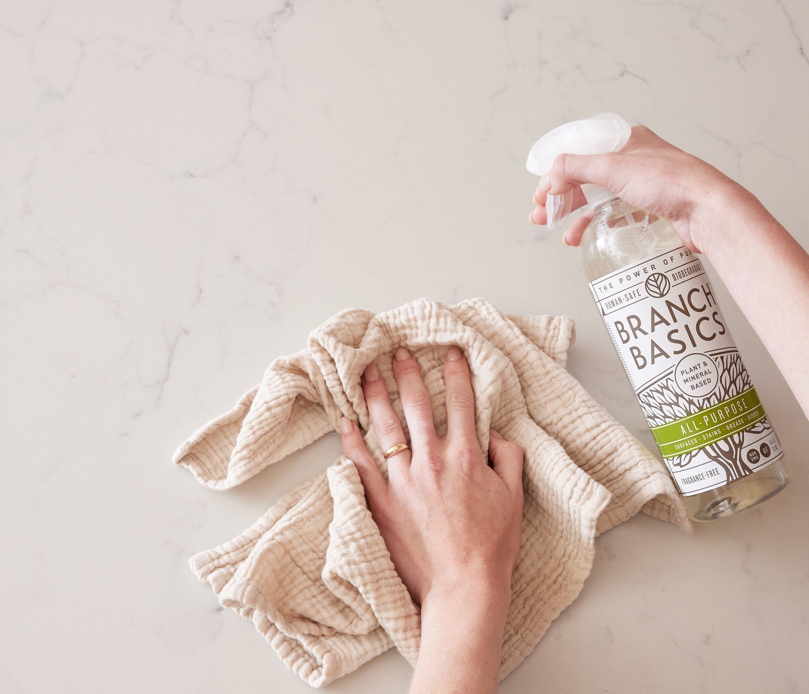 A person is holding a Plastic All-Purpose Spray bottle in one hand and a cloth hand towel in the other, using both to clean a stone countertop. - View 4
