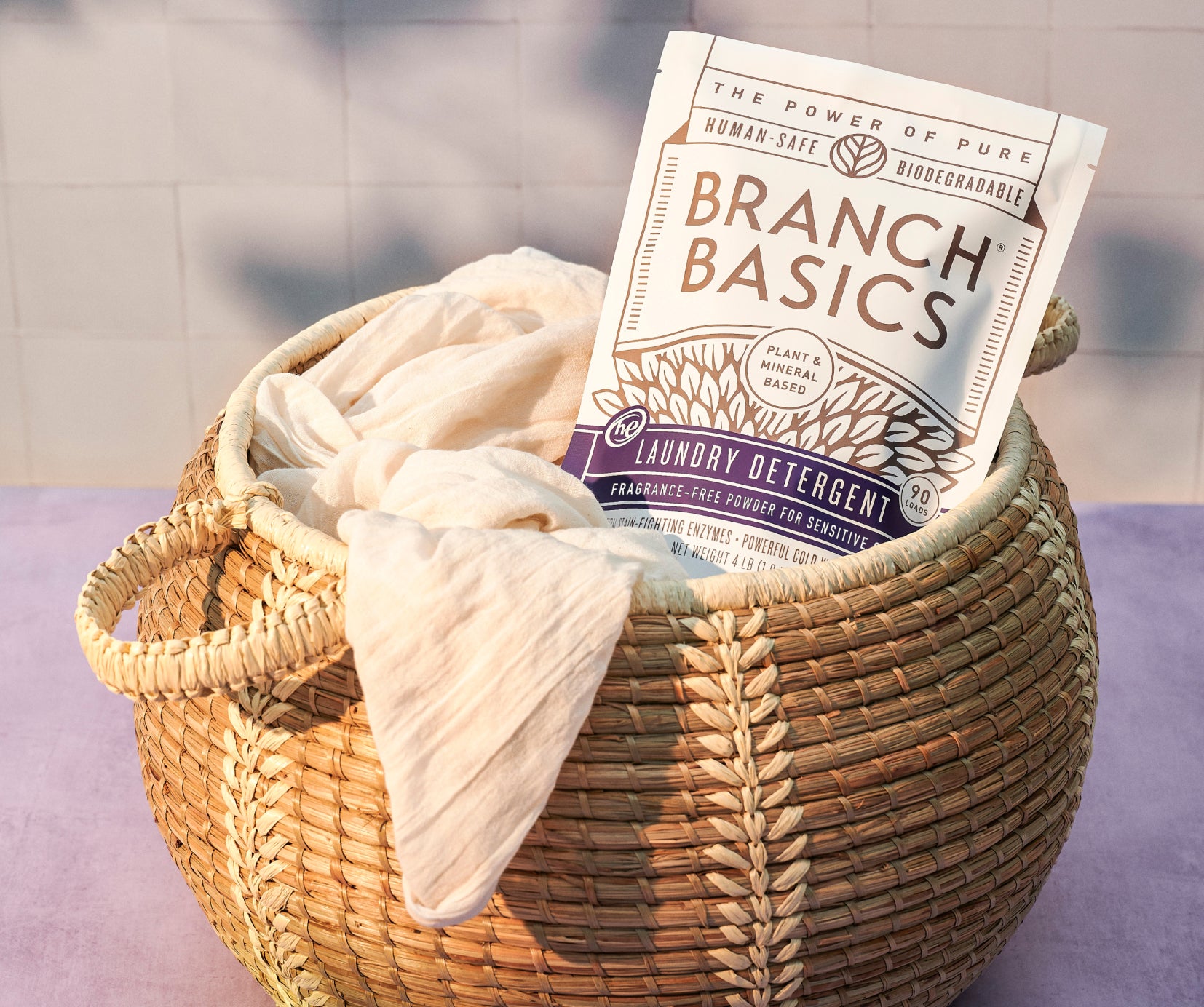 A pouch of Branch Basics Laundry Detergent tucked into a full laundry basket. - View 5
