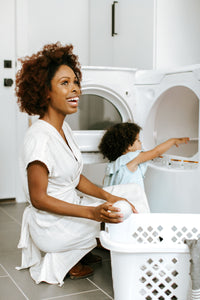 An adult and child in front of an open clothes dryer, with the adult holding a single Wool Dryer Ball in their hand. - Thumbnail View 5
