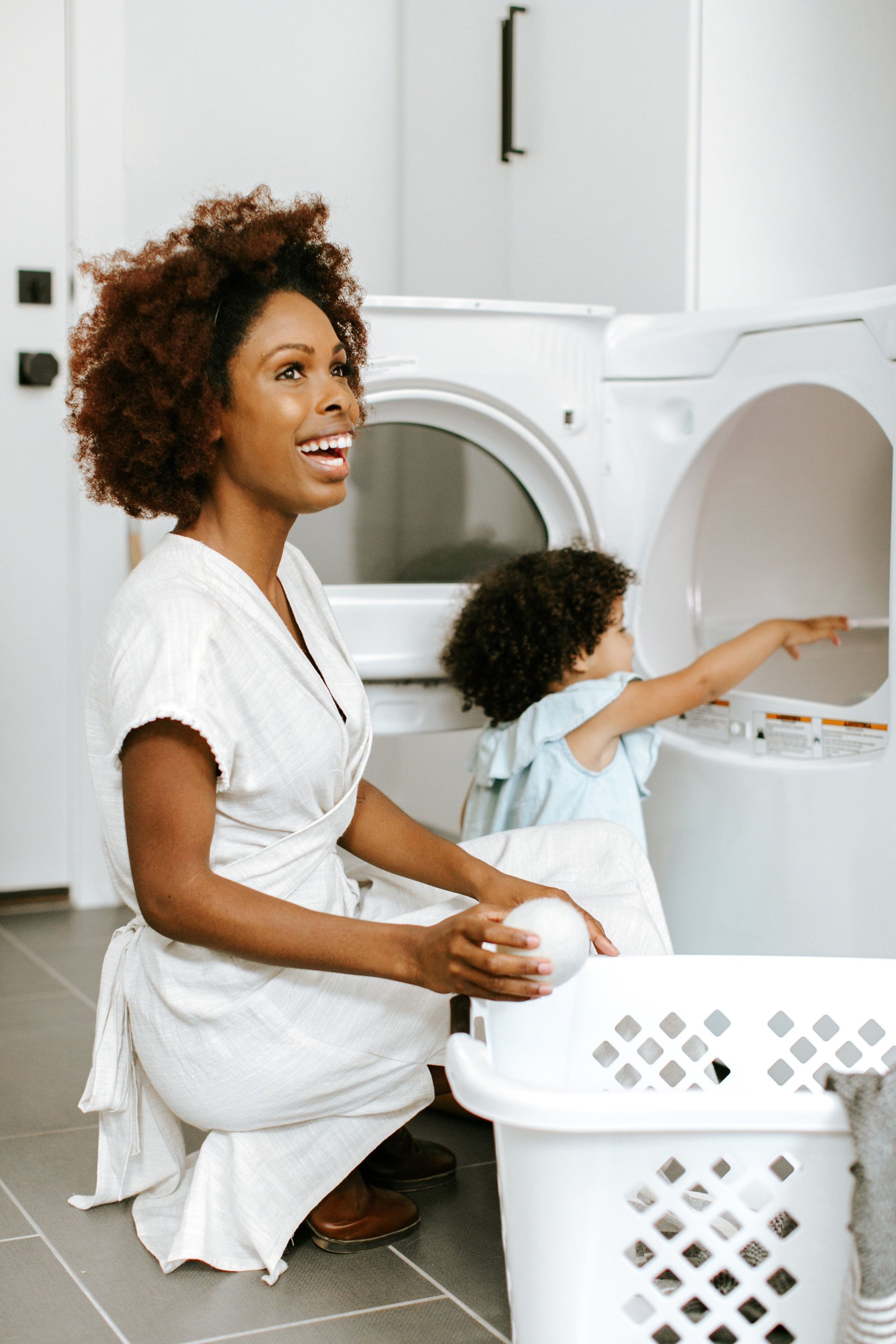 An adult and child in front of an open clothes dryer, with the adult holding a single Wool Dryer Ball in their hand. - View 5
