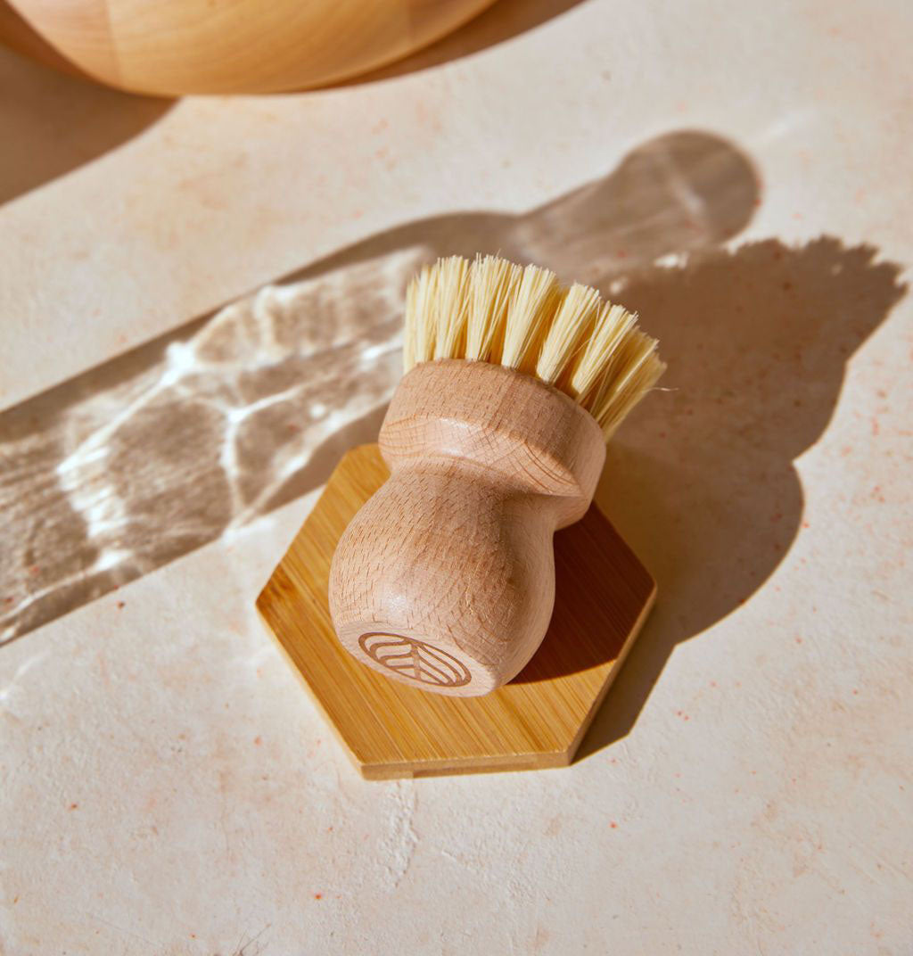 A Natural Scrub Brush, made with a solid beechwood handle and natural fiber bristles, displayed on an elevated wooden tray and neutral background. - View 3
