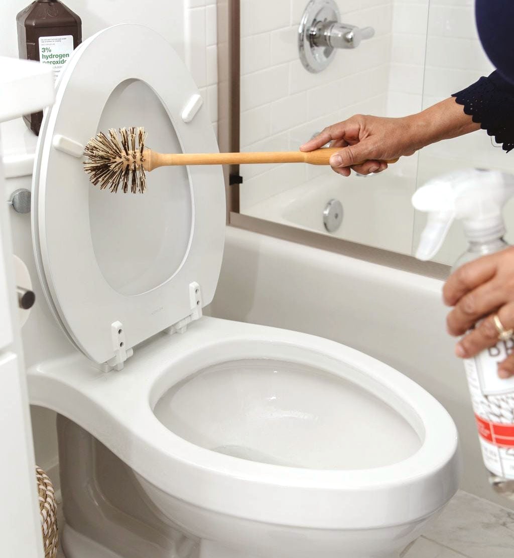 A person scrubs a toilet with an abrasive brush in one hand, while the other hand holds a refillable Plastic Bathroom bottle in the foreground. - View 4
