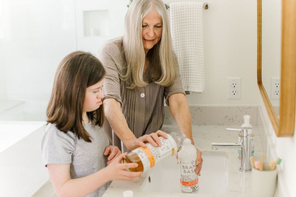 An adult and child standing at a sink and working together to refill a Plastic Bathroom bottle with Branch Basics Concentrate and water. - View 3

